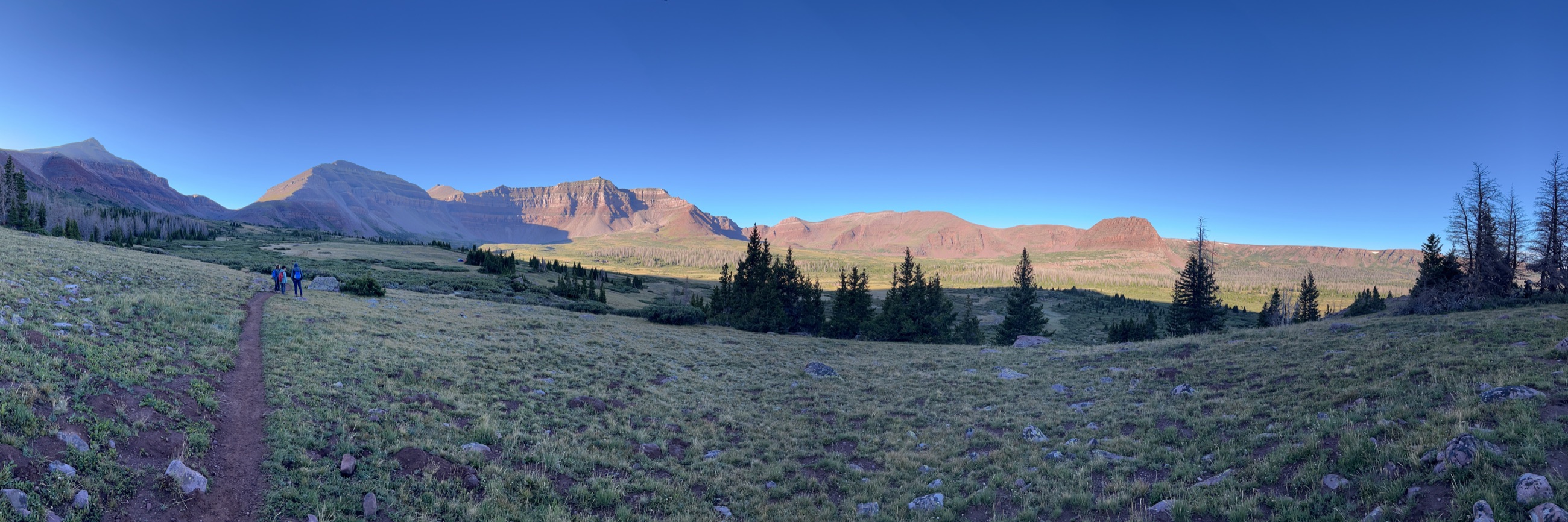 A trail crossing a broad alpine basin beneath red mountain ridges